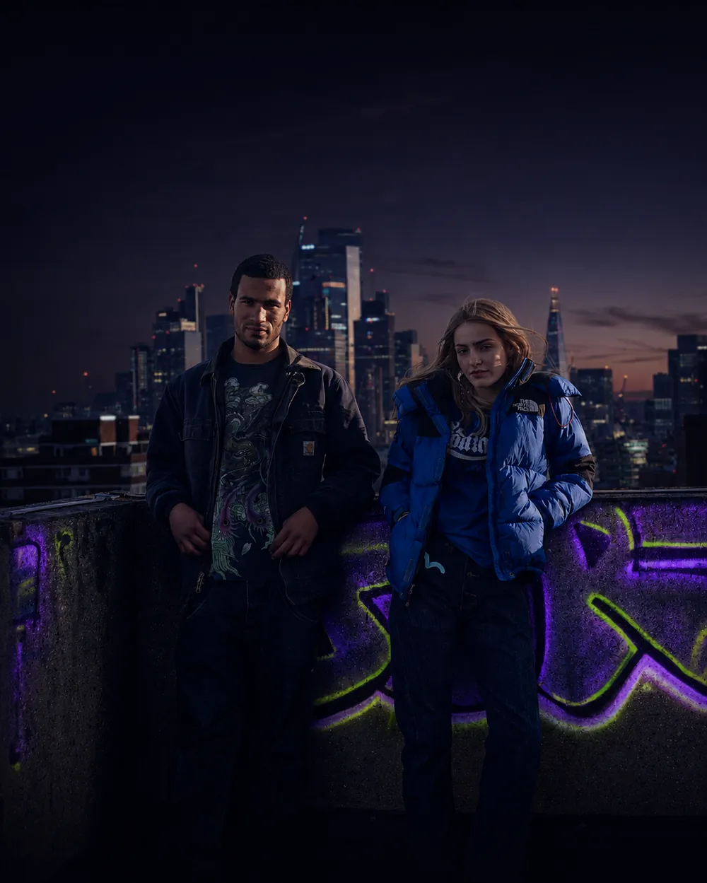 Two people in vintage workwear on a rooftop above the city at dusk
